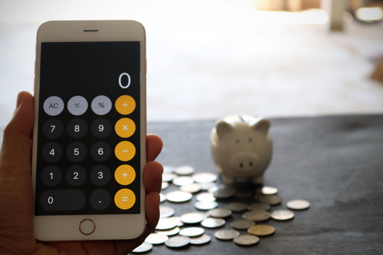 iphone em calculadora com cofre de porquinho e moedas ao fundo