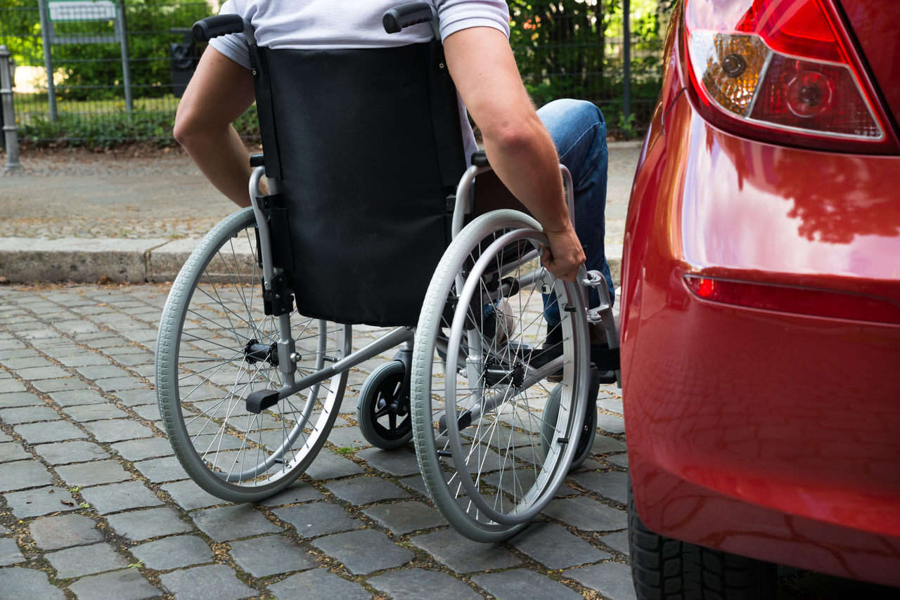 motorista sentado em cadeira de rodas ao lado do carro estacionado