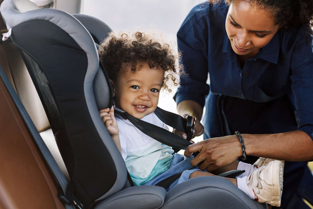 mãe coloca o cinto de segurança em seu filho no assento infantil de carro
