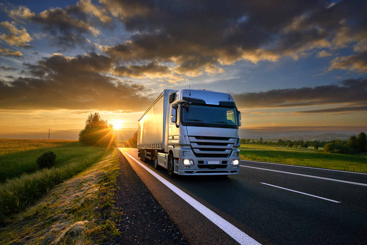 imagem de caminhão de carga em rodovia com pôr do sol ao fundo